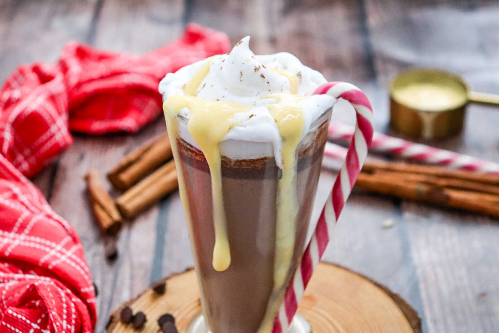 Creamy eggnog hot chocolate with whipped cream and eggnog drizzle in a festive glass mug.