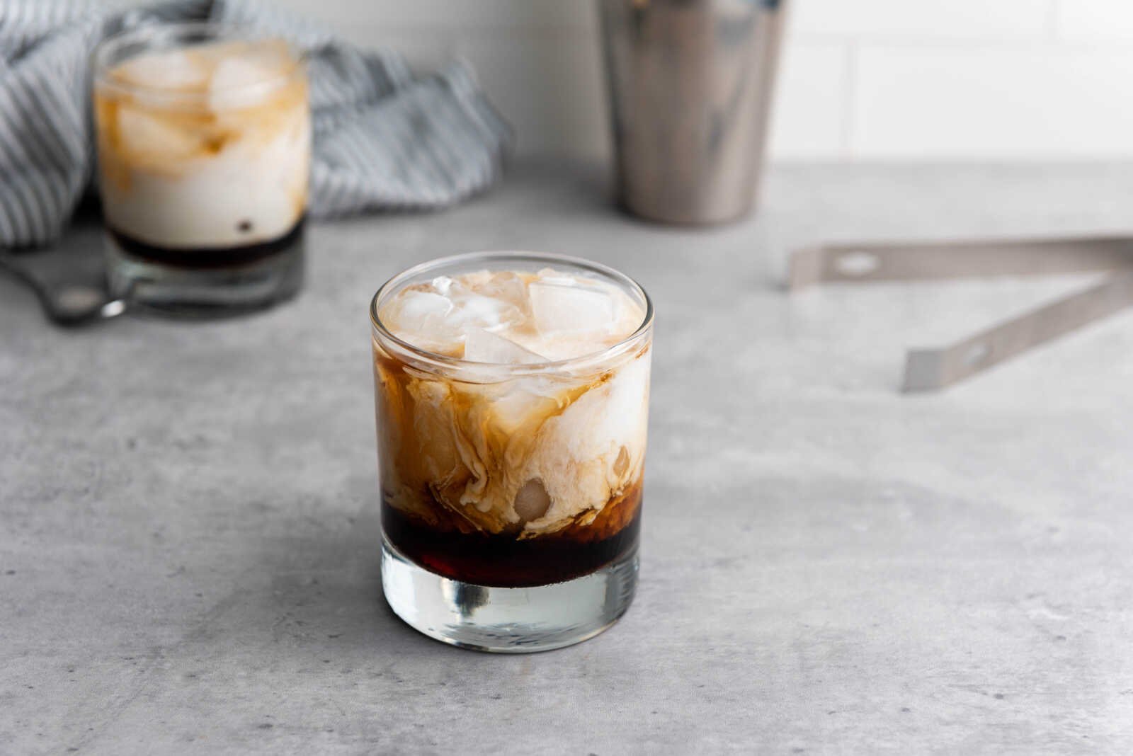 White Russian Cocktail with cream swirling into coffee liqueur and vodka over ice in a rocks glass.